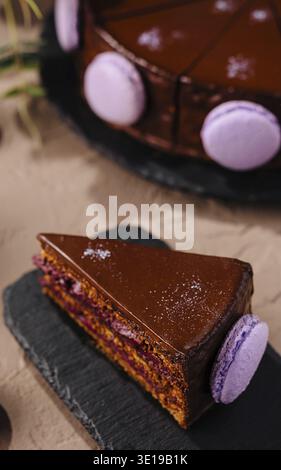 Ein Stück reichhaltiger Schokoladenkuchen serviert mit lila Macarons und Tee, elegante Dessert-Einrichtung Stockfoto