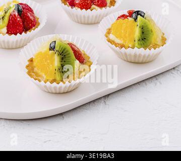Elegante Törtchen mit Kiwi-, Orangen- und Erdbeerscheiben auf Keramikplatte Stockfoto
