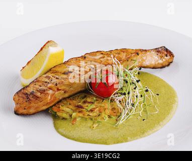 Köstlich gegrilltes Lachsfilet, serviert mit einer lebendigen grünen Sauce, Zitrone und frischer Beilage Stockfoto