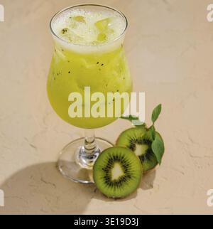 Gekühlter Kiwi-Cocktail mit frischer Obstgarnitur, serviert auf einer sonnendurchfluteten Sandoberfläche Stockfoto