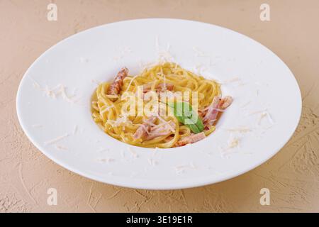 Cremige Carbonara-Pasta, serviert auf einem weißen Teller, abgeschmeckt mit geriebenem Parmesan und garniert mit Basilikum Stockfoto