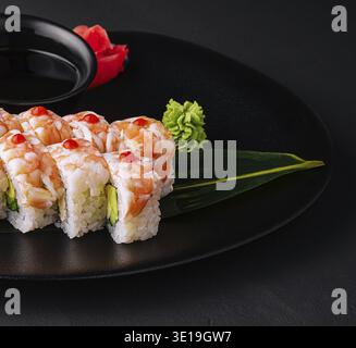 Sushi-Rolle bedeckt mit Garnelenfleisch auf schwarzer Keramikplatte Nahaufnahme Stockfoto