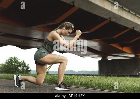 Eine athletische Frau, die während ihres Street Workouts mit einem Widerstandsgummi Ausfallschritte macht Stockfoto
