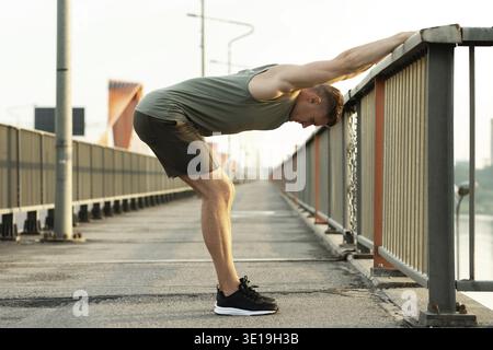 Junger, sportlicher Mann, der sich vor seinem Straßenkraining auf der Brücke aufwärmt Stockfoto