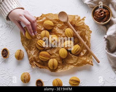 Eine Hand, die nach frisch gebackenen, nussförmigen Keksen mit Karamell greift Stockfoto