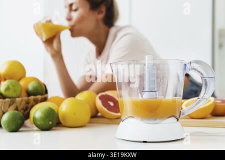 Nahaufnahme von Zitruspresse und Frau, die frisch gepressten hausgemachten Orangensaft trank Stockfoto