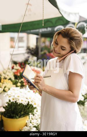 Junge und schöne Frau Floristin, die telefonisch in ihrem kleinen Blumenladen bestellt Stockfoto
