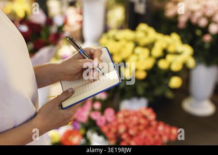 Bestellungen im Blumenladen. Eine Floristin macht Notizen in ihr Notizbuch Stockfoto