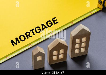 Hypothek. Finanzgeschäftskonzept. Hölzerne Miniaturen von Häusern und das Wort HYPOTHEK in Gelb auf grauem Hintergrund. Kopierbereich Stockfoto