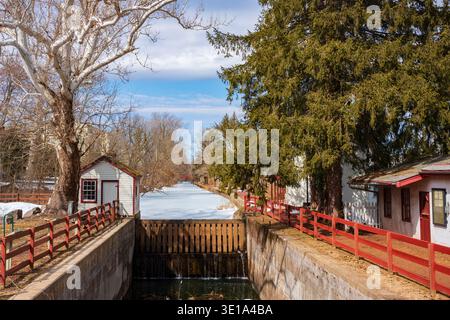 Ein schneebedeckter Kanal und eine blattlose Birke leuchten an einem kalten Wintertag im Sonnenlicht über einem Schleppweg und dem Delaware Canal Trail. Stockfoto