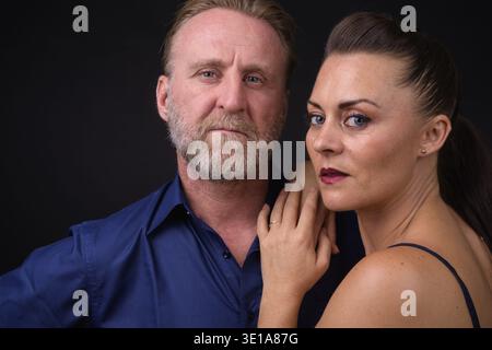 Studio-Aufnahme von reifem, gutaussehendem bärtigen Mann und reifer, schöner Frau zusammen vor schwarzem Hintergrund Stockfoto
