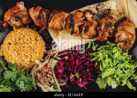 Hähnchenshish Kebab mit Bulgur, Gemüse und Pita-Brot auf schwarzer Platte Stockfoto