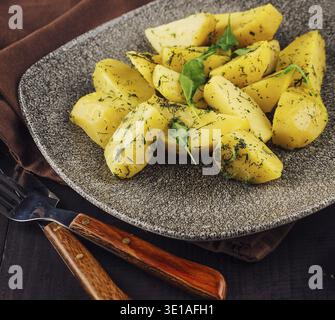 Gebackene Kartoffelscheiben mit Dill und Kräutern auf grauer Platte auf dunklem Holztisch Stockfoto