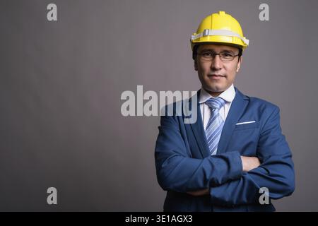 Studio geschossen von jungen asiatischen Geschäftsmann, tragen, hardhat gegen grauer Hintergrund Stockfoto