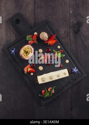 Köstliches Gourmet-Dessert wird auf einem Schieferbrett serviert, mit frischem Obst, einer Schaufel Eis und einem wunderschön überzogenen Gebäck Stockfoto