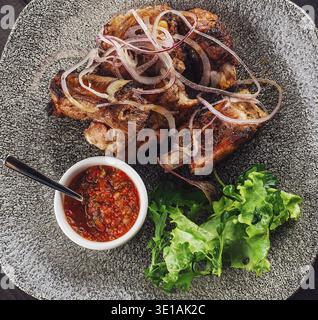 Gegrillte Schweinerippchen mit Zwiebelringen und Sauce serviert auf einem Teller mit frischem Salat und Tomatensoße Stockfoto