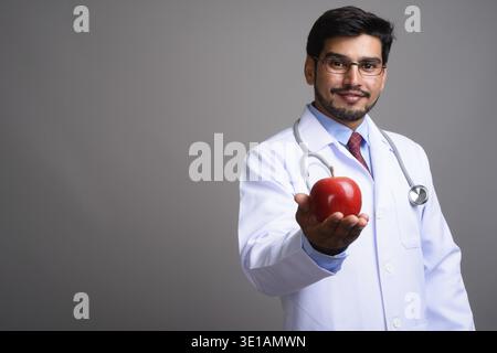 Studio shot der Jungen gut aussehenden bärtigen Persischen mann Arzt tragen Brillen gegen grauer Hintergrund Stockfoto