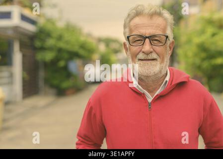 Glücklich aussehenden älteren bärtigen Mann lächelnd beim Tragen von Brillen und rote Jacke im Freien Stockfoto