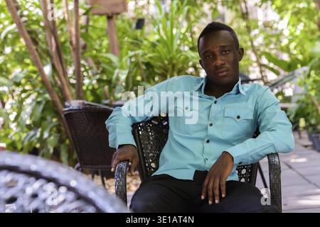 Jungen schwarzen afrikanischen Mann an outdoor Café mitten in der Natur sitzen Stockfoto