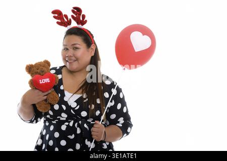Studio shot der Jungen gerne Fett asiatische Frau lächelnd, während sie Teddybär mit Herz und Liebe Zeichen beim Tragen von Rentier Kopfbügel und halten roten b Stockfoto