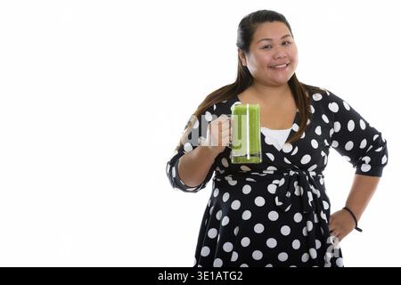 Studio shot der Jungen gerne Fett asiatische Frau lächelnd, während sie Glas grünes Gemüse smoothie Stockfoto