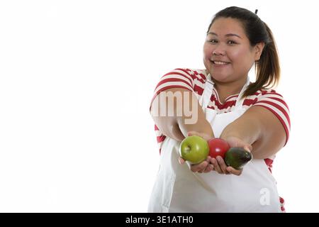 Studio shot der Jungen gerne Fett asiatische Frau lächelnd, während Sie eine frische Früchte und Tragen einer Schürze Stockfoto