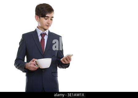 Studioaufnahme eines jungen, hübschen persischen Teenagers, der Kaffee hält tasse und mit Handy Stockfoto
