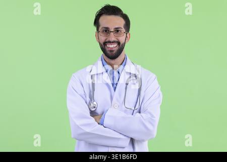 Studio-Aufnahme eines jungen gutaussehenden, bärtigen persischen Mannes Doktor vor grünem Hintergrund Stockfoto