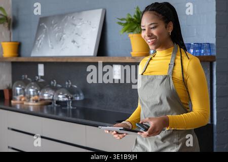 Afroamerikanerin, die ein Tablet benutzt, Leser am Café-Theke mit Schürze, Senfplatte, Kopierraum Stockfoto