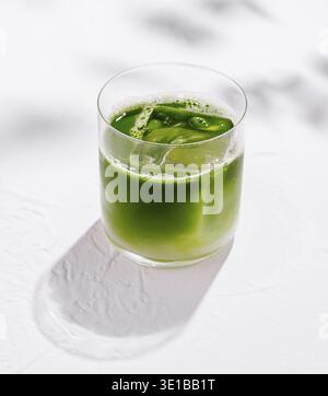 Erfrischende Eismatcha Latte sitzt auf einem weißen Tisch mit Schatten von Blättern im Hintergrund Stockfoto