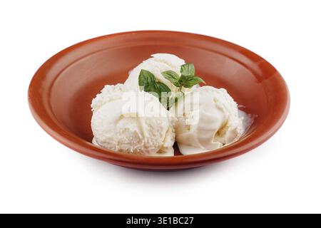 Drei Kugeln Vanilleeis schmelzen in einer rustikalen, braunen Schüssel, gekrönt mit einem Minzzweig Stockfoto