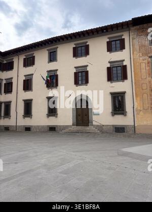 Biblioteca Del Dipartimento Di Diritto Pubblico. Pisa, Italien. Institutionelles Gebäude mit Fensterläden und italienischen Fahnen, die unter einem bewölkten Himmel fliegen Stockfoto