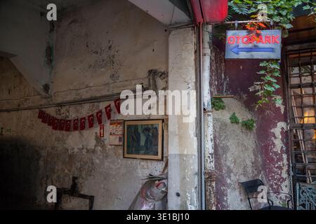 Abgenutzter Innenhof mit abblätternden Wänden, türkischen Fahnen, gerahmter Kunst und einem Neonschild, das rustikalen urbanen Verfall und lokalen Charakter einfängt Stockfoto