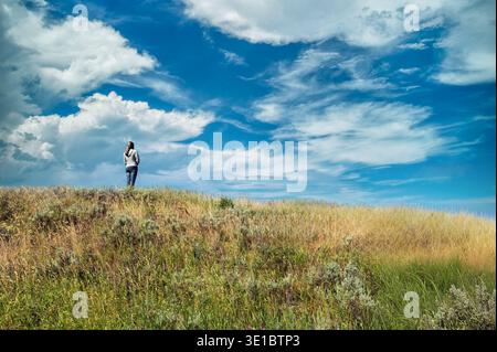 Die Frau steht allein auf einem Hügel und bewundert die Schönheit der Wolken und ist in Gedanken verloren. Konzeptuelles Bild der Bewunderung der Natur oder der Gedanken über Gott Stockfoto