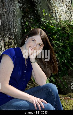 Die junge Frau ruht neben einer Live Oaks in Louisiana. Ihr Haar weht in der Brise. Sie trägt Jeans und blaues Hemd. Stockfoto