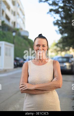 Porträt einer schönen, Reifen Frau, die mit überkreuzten Armen auf der Straße lächelt Stockfoto