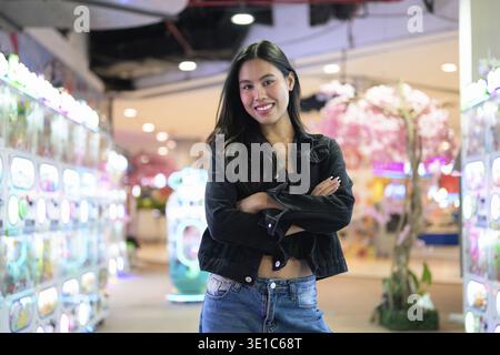 Glückliche junge asiatische Frau, die drinnen Arcade-Videospiele spielt Stockfoto