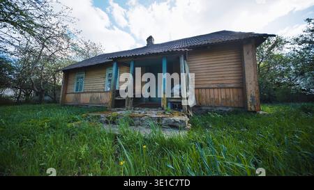 Verlassenes altes Holzhaus mit Veranda auf bewachsenem grünem Gras in ländlicher Szene Stockfoto