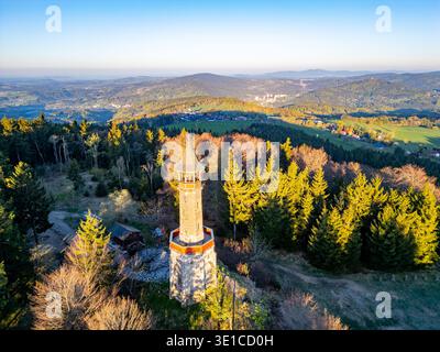 Der Stepanka-Aussichtsturm steht hoch inmitten von frischem Grün in Korenov, Isergebirge. Die frühe Sonne beleuchtet die Umgebung und offenbart einen ruhigen Frühlingsmorgen. Stockfoto