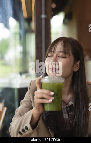 Junge asiatische Frau trinkt grünen Entgiftungssaft im Café Stockfoto