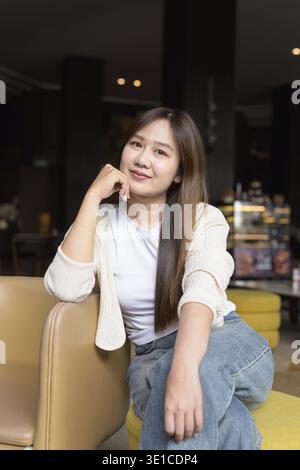 Junge asiatische Geschäftsfrau, die im Café-Restaurant sitzt, lächelt und in die Kamera schaut Stockfoto
