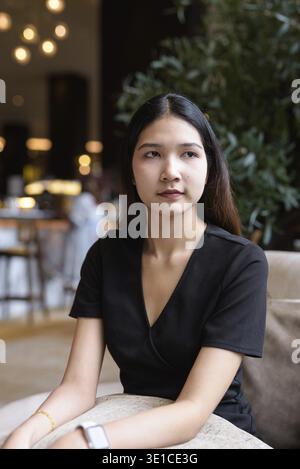 Junge asiatische Frau, die im Café sitzt und ein stilvolles schwarzes Kleid trägt Stockfoto