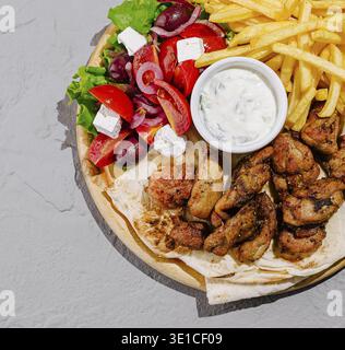 Eine lebendige Platte mit gegrilltem Hühnchen, frischem Gemüse, Pommes frites und Tzatziki-Sauce. Der farbenfrohe Salat umfasst Tomaten, Salat und Oliven Stockfoto