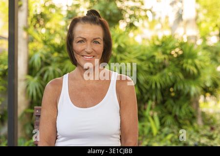 Glückliche Frau lächelt und sitzt draußen während des Sommerkonzepts Stockfoto