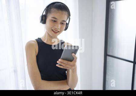 Fitness asiatische Frau mit Smartphone und Kopfhörern genießt Musik. Frau mit Kopfhörer Smartphone nach dem Training Stockfoto