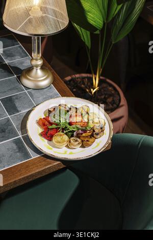 Auf einem schönen Teller steht ein lebhaftes Sortiment an gegrilltem Gemüse, einschließlich Zucchini und Auberginen, garniert mit Kräutern. Die warme Atmosphäre ist en Stockfoto