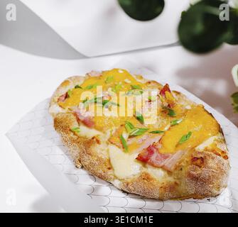 Dieses köstliche gebackene Produkt besteht aus einer knusprigen Kruste mit geschmolzenem Käse, Schinken und frischen Kräutern. Perfekt auf dekorativem Papier serviert, sehr gut Stockfoto
