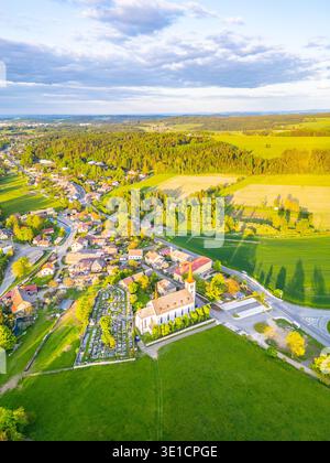 Bohutin Town bietet eine malerische Landschaft mit üppigen Feldern und malerischen Häusern. Die historische Kirche und der Friedhof sind markante Elemente, die vom warmen Glanz des Sonnenuntergangs beleuchtet werden. Stockfoto