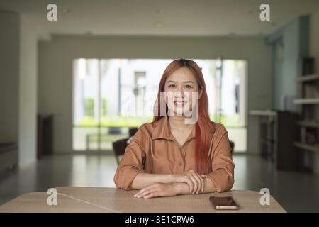 Porträt der schönen jungen asiatischen Frau, die drinnen im Coworking Space Style Library Office sitzt Stockfoto