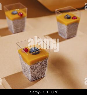 Drei Chia Pudding Desserts mit Mangopüree garniert mit Beeren, stilvoll präsentiert Stockfoto